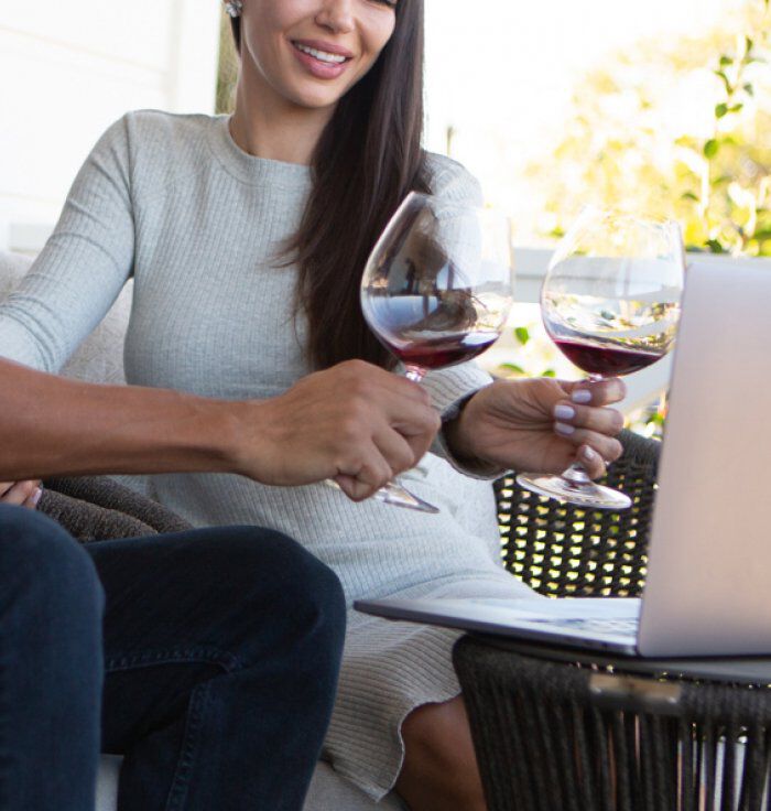 Two People Holding Red Wine in Glass in Front of Laptop Screen